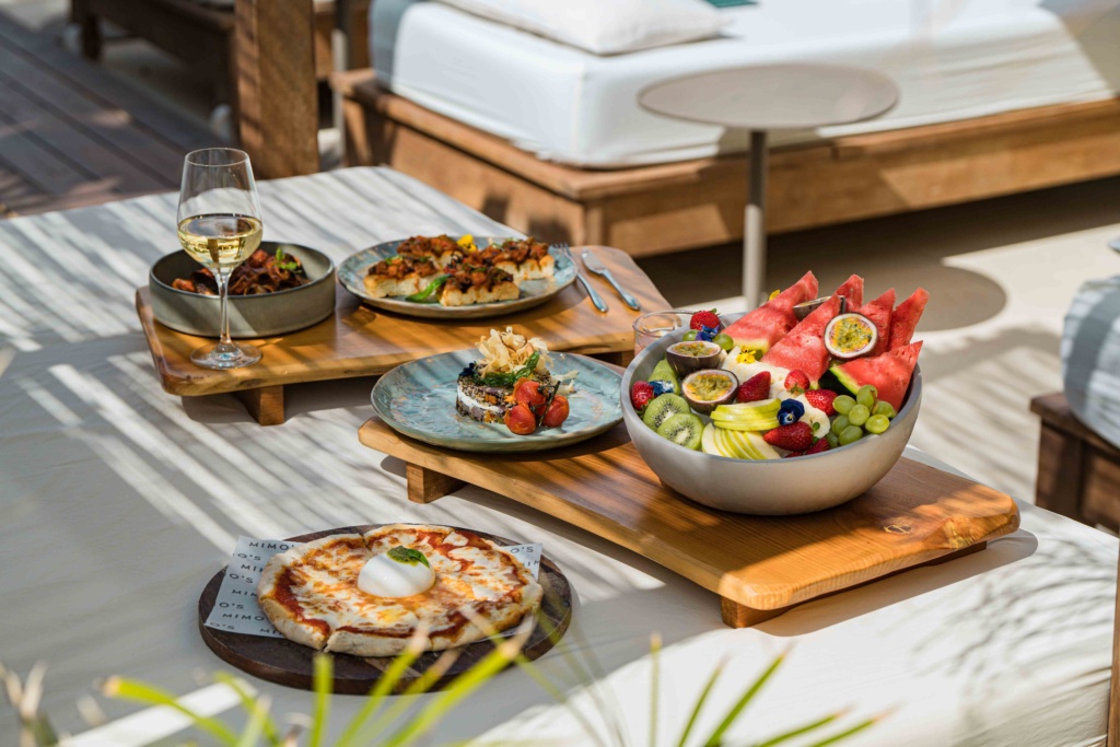 Una combinación deliciosa de frutas tropicales, pizza, platos gourmet y una copa de vino blanco